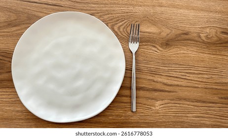 Empty White Ceramic Plate And Stainless Steel Fork On Wooden Table, Top View, Daylight, Concept Of Minimalist Dining, Table Setting, Food Background, Restaurant, Fasting, Healthy Eating