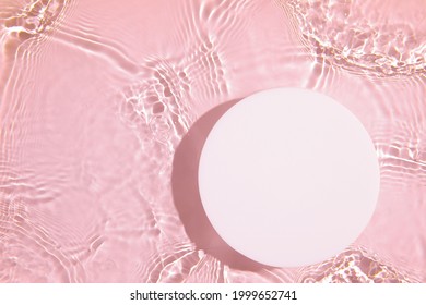 Empty white circle podium on transparent clear pink calm water texture with splashes and waves in sunlight. Abstract nature background for product presentation. Flat lay cosmetic mockup, copy space.