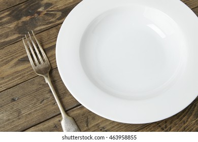 An empty white dinner plate and fork on a reclaimed wooden background - Shutterstock ID 463958855