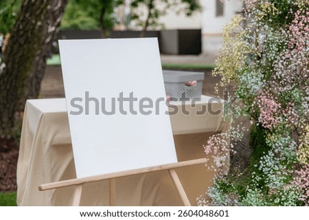 Empty white easel for text and drawing on a background of a garden with flowers. Mockup for artist's creativity