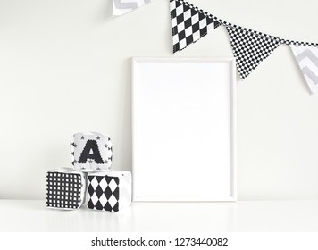 Empty White Frame Mockup For Artwork, Painting, Posters Or Photo, Monochrome Nusery Interior With Blank Frame, Flags Bunting And Soft Baby Blocks.