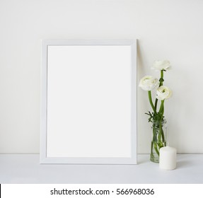 Empty white frame with place for text on the white wall and table, bouquet of flowers ranunculus and candle. Scandinavian style room interior. Template mock up for paintings or photographs. - Shutterstock ID 566968036
