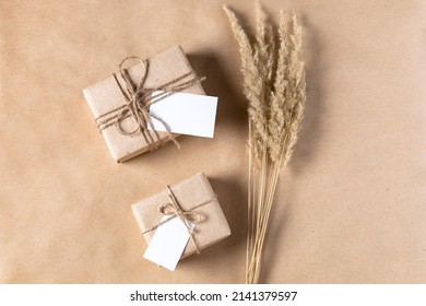 Empty White Gift Tag Mock Up On Craft Paper Box With Dried Spikelets Decoration On Beige Background. Flatlay, Top View With Copyspace, Mock Up. Minimal Boho Style