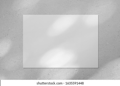 Empty white horizontal rectangle poster or business card mockup with diagonal dappled light spots on gray concrete wall. Flat lay, top view. For advertising, brand design, stationery presentation.