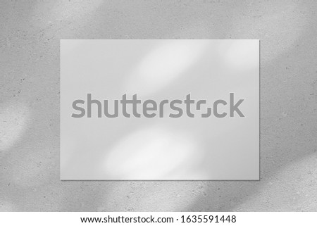 Empty white horizontal rectangle poster or business card mockup with diagonal dappled light spots on gray concrete wall. Flat lay, top view. For advertising, brand design, stationery presentation.