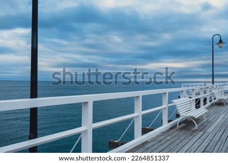 Empty white Old wood bridge pier against beautiful sunset sky natural background, backdrop wallpaper multipurpose sea scene. White benches no people in Gdynia Orlowo, Poland. Touristic destination
