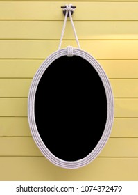 Empty White Oval Frame Covered with White Ropes Hanging on Yellow Wooden Panel Wall used as Template to mock up photo or input text