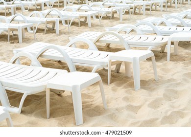 Empty White Plastic Deck Chairs On Sandy Beach