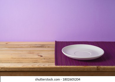 Empty White Plate With Bamboo Mat On Wooden Table Over Purple Background. Kitchen Or Restaurant Counter Mockup For Design