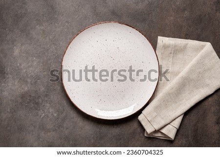 Empty white plate with a beige linen napkin on a brown rustic background. Top view, flat lay, copy space.