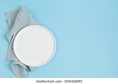 Empty white plate and cotton napkin on blue backdrop. Food background for menu, recipe book. Table setting. Flatlay, top view, mockup