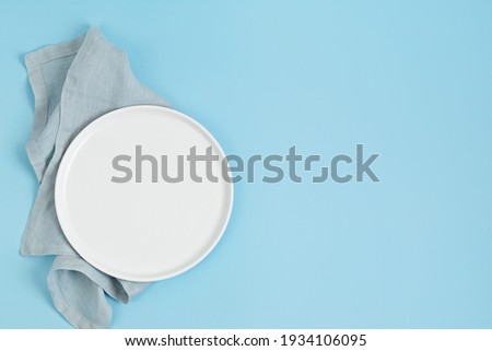 Empty white plate and cotton napkin on blue backdrop. Food background for menu, recipe book. Table setting. Flatlay, top view, mockup