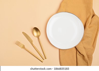 Empty White Plate, Golden Cuterly And Cotton Napkin On Beige Backdrop. Food Background For Menu, Recipe Book. Table Setting. Flatlay, Top View, Mockup