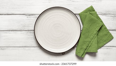 Empty white plate with green napkin on white wooden background. Top view, flat lay. Banner.
