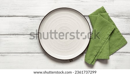 Empty white plate with green napkin on white wooden background. Top view, flat lay. Banner.