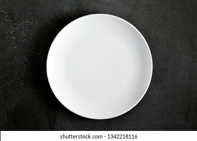 Empty white plate on black background table. Flat lay, top view, copy space