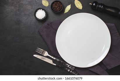 Empty White Plate On Black Stone Table And Napkin. Food Background For Menu, Recipe. Table Setting. Flatlay, Top View. Mockup For Restaurant Dish