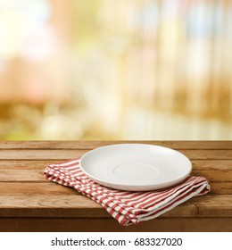 Empty white plate on wooden table over blurred bokeh background