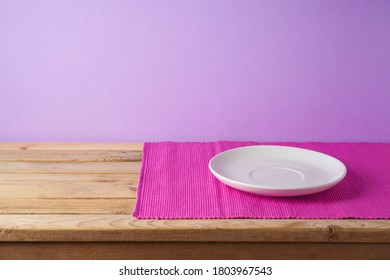 Empty White Plate With Pink Mat On Wooden Table Over Purple Background. Kitchen Or Restaurant Counter Mockup For Design