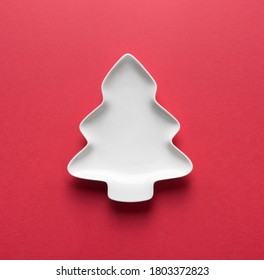 Empty White Plate In Shaped Of Christmas Tree On Red With Space For Design. Xmas Greeting Card. View From Above.