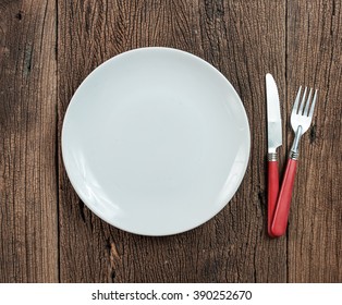 Empty White Plate With Silverware On Wooden Table. View From Above