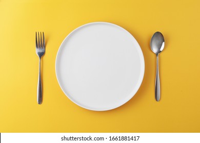 Empty white plate with spoon and fork on yellow background. Meal preparation concept.
