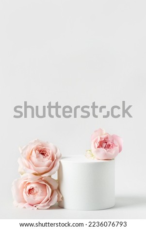 Empty white podium and pink roses on light grey background. Minimal cosmetic template. Round showcase for product marketing. Abstract display or stage. Spa and beauty concept. Still life. Copy space.