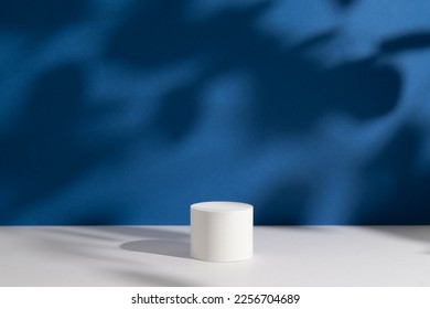 Empty white round podium and deep shadows on dark blue background. Showcase for product presentation. Pedestal for beauty cosmetic advertising. Minimal still life. Front view.