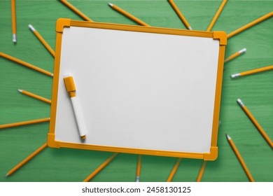 Empty white school board. Copy space. Top view. Whiteboard on background of green wooden table with scattered orange pencils. Template for design with place for text. concept of business, education.