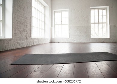 Empty white space in fitness center, white brick walls, natural wooden floor and big windows, modern loft studio, unrolled yoga mat on the floor, comfortable open area for sport and exercises