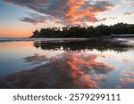 Empty wide sandy beach during high tide at sunset hour with the colorful sky and clouds fully reflecting in the shallow water. El Cuco, El Salvador.