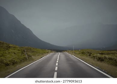 Empty winding road through dramatic highland landscape in Glencoe Scotland under dark atmospheric skies.