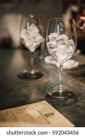 Empty Wine Glass With Ice Cubes On Metal Table In Bar. Close Up View Blur In Background