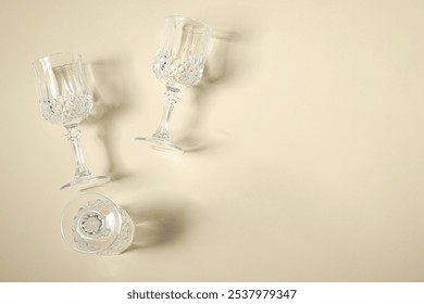 Empty wine glasses casting beautiful shadows on beige background, flat lay. Space for text