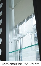Empty Wine Glasses Stand On A Glass Shelf By The Window, A Blue Sky In The Background. Decorative Background For Bar Or Kitchen Advertising
