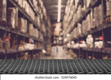 Empty wire mesh table on defocuced blurred boxes on rows of shelves in warm light warehouse background.