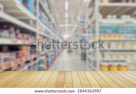 Empty wood table with blurred paint cans on shelves in large hardware store background.