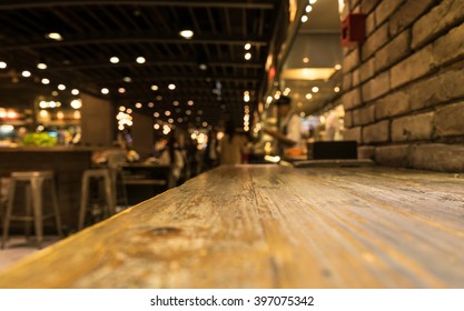 Empty Wood Table Top Of Bar With Blur Of Cafe Restaurant In Dark Night Background/selective Focus .For Montage Product Display