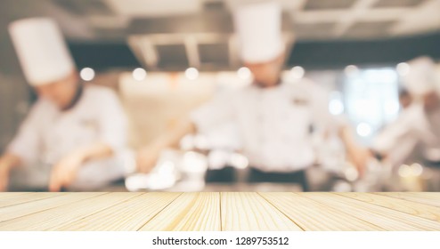 Empty Wood Table Top With Chef Cooking In Restaurant Kitchen Blurred Defocused Background