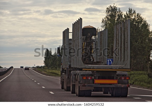 Empty wood truck drive with a trailer on a\
suburban asphalt highway road on summer evening, timber transport,\
forestry business