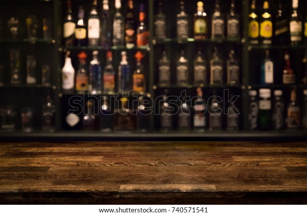 Empty wooden bar counter with defocused\
background and bottles of restaurant, bar or cafeteria background\
/for your product display