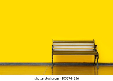 Empty wooden bench at garden park, with yellow wall background  Alone and lonely concepts.