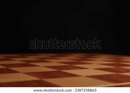 Empty wooden chess board against black background, closeup. Space for text