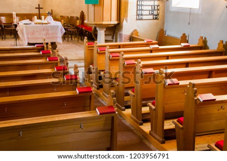 Empty wooden church benches of a Christian church with bible or choir books with cross . Blurry alter in the background. Selective focus. Concept of church service or empty churches.