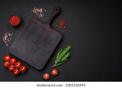 Empty wooden cutting board with cherry tomatoes, spices, salt and herbs on dark concrete background - Powered by Shutterstock