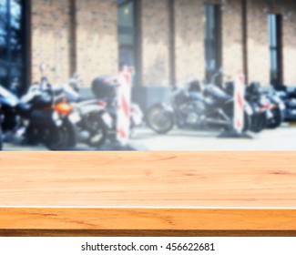 Empty wooden deck table over  burred of motorbikes  in front of old brick wall  shop background for product montage display.