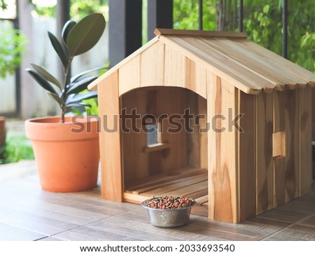 Empty wooden dog's house with dog food bowl  in balcony decorated with houseplant in plant pot.