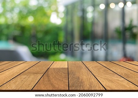 Empty wooden in front of blurred background of  the glass building and the beautiful atmosphere outside the restaurant and cafe decorated with a large pond and green trees give a feeling of freshness.