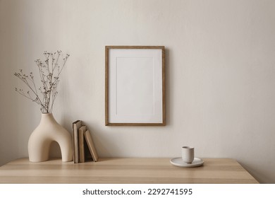 Empty wooden picture frame mockup hanging on beige wall background. Boho shaped vase, dry flowers on table. Cup of coffee, old books. Working space, home office. Art, poster display. Modern interior.