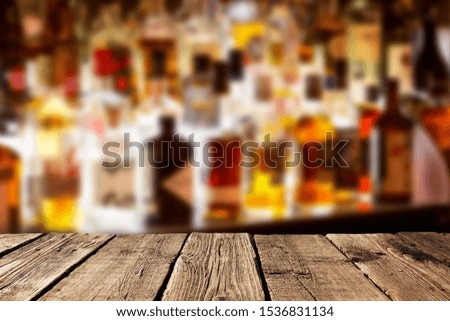 Empty wooden planks against various alcohol bottles in a bar or restaurant. Bar advertisement mockup image